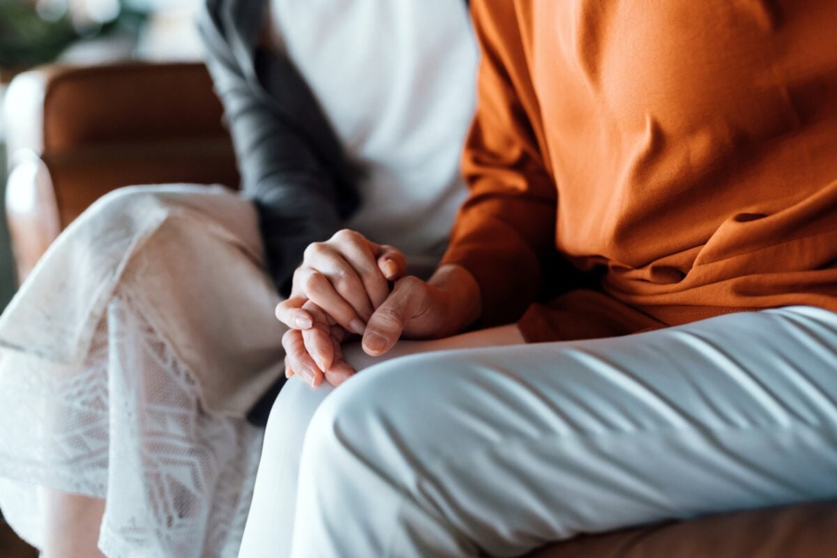 Two women sitting on a couch, holding hands, sharing a moment of connection during dementia care.