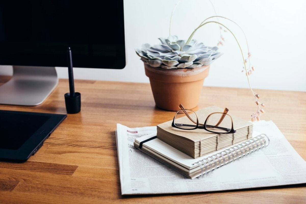A neat desk holding a computer, notebook, and potted plant, symbolizing dealing with the challenges of disability in the workplace.