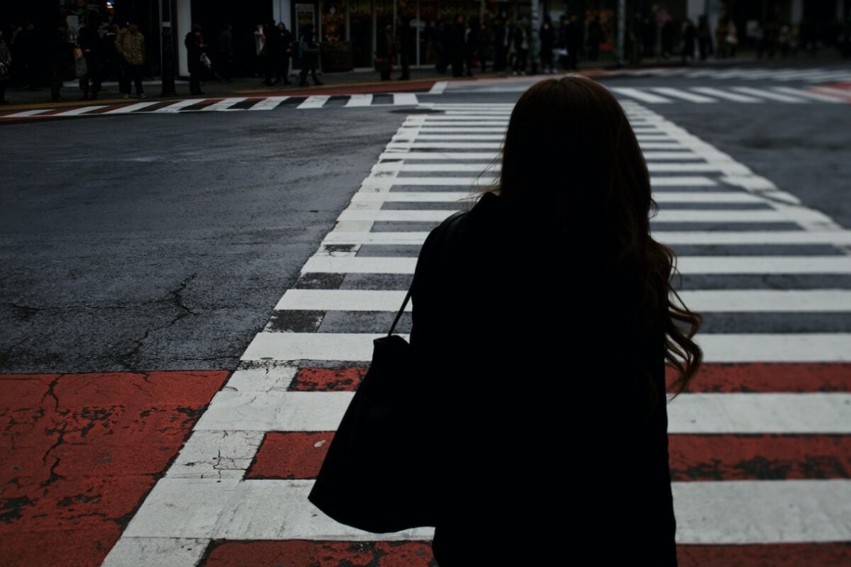 A woman stands on a city crosswalk, hesitant about walking towards a crowded sidewalk, highlighting the detachment of schizoid personality disorder.