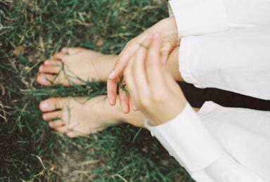 A woman drops blades of grass from one hand to another above her bare feet, illustrating the unusual behavior of schizotypal personality disorder.