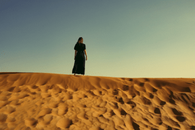 A woman on a sand dune surveys the desert, her silhouette framed against the bright sky, suggesting histrionic personality disorder.