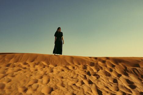 A woman on a sand dune surveys the desert, her silhouette framed against the bright sky, suggesting histrionic personality disorder.