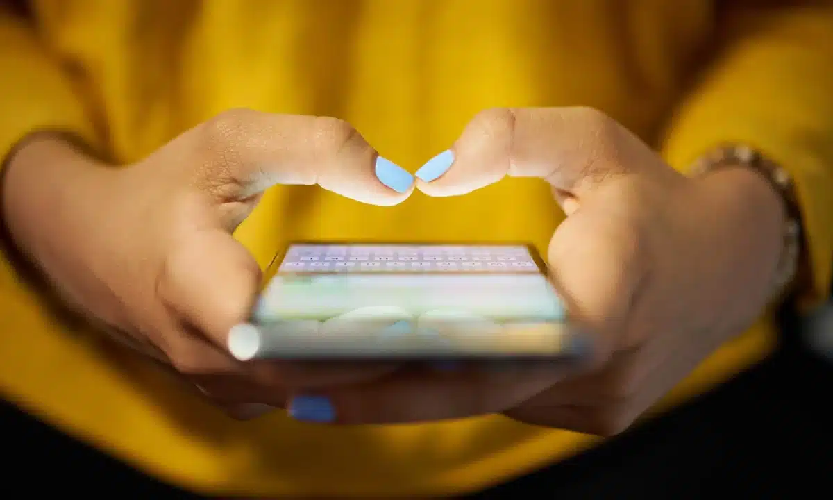 Woman in yellow top obsessively using her phone, highlighting the link between social media and mental health.